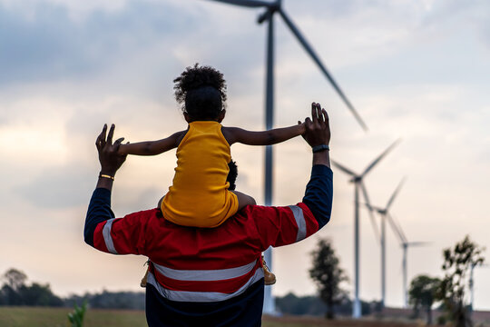 Black african father engineer holds his daughter in his arms at the wind turbines with great freedom. Concept of environmental engineering, renewable energy and love for nature and for the family