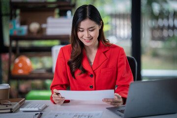  Attractive young smiling Asian woman in smart casual wear and holding smart phone looking at camera while leaning on desk in creative office Confident business expert