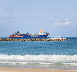 The sand pumping vessel sails along the breakwater close to the coastline