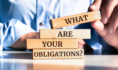 Close up on businessman holding a wooden block with "What are your obligations?" message