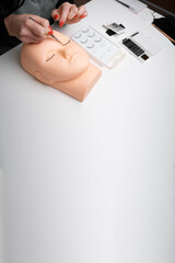Obraz premium A beauty mannequin training head with a woman practicing lash extension techniques. Training eyelash extensions concept. Copy space