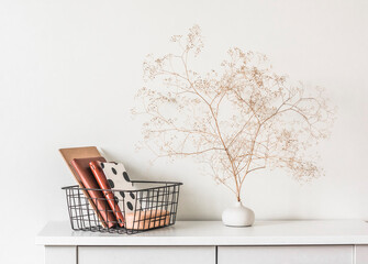 Minimalism interior - black metal basket with notebooks and natural decor on a white table in the...