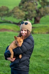 girl on a farm holding a puppy dog in her arms, tan kelpie puppy