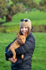 girl on a farm holding a puppy dog in her arms, tan kelpie puppy