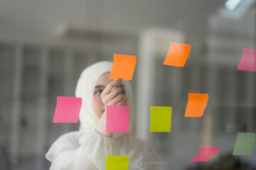 A Muslim businesswoman uses Post-it notes to share ideas, showcasing the concept of brainstorming....