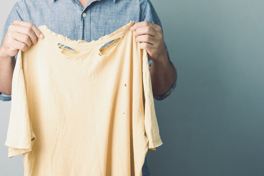 Used wrong type of washing powder concept. Man holding yellow torn and old T-Shirt. Studio shot on grey wall.