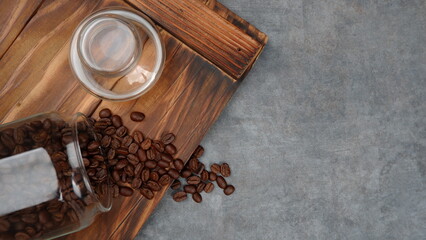 Fototapeta na wymiar Photography of coffee beans spilling from a jar, on pieces of wood with a gray background, suitable for photos of food and beverage products, with landscape photo format