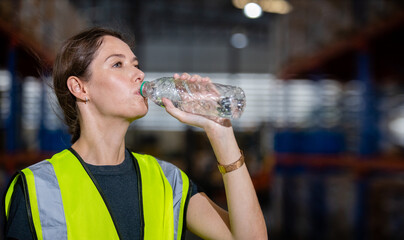 Women engineer drinking water from plastic bottle after working at factory during break. Drinking...