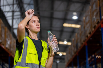 Women engineer drinking water from plastic bottle after working at factory during break. Drinking...