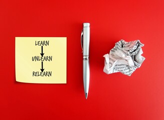 Pen, crumpled paper and note paper on red background with handwritten text Learn Unlearn Relearn - means knowing to discard learned outdated knowledge skills information and ready to relearn new ones