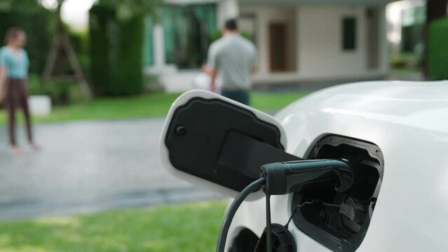 Progressive Parent Have Returned From Picking Up Daughter At School With Concept Of Electric Vehicle And Renewable Energy, Charging Station For EV Car At Home. Alternative Eco Transportation.