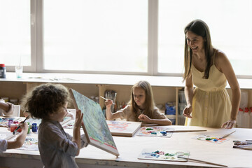 Art school pupil kid showing new abstract artwork to cheerful teacher. Group of kids learning...
