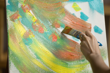 Hand of young woman touching canvas with paintbrush. Artist painting abstract picture, applying colorful strokes, drawing artwork in acrylic paints, oil. Close up cropped shot of arm