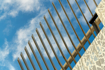 Metal building facade with ribbed beams reaching out to blue cloudy sky afternoon sunlight white hole punched exterior