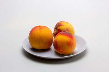 Fruits of ripe peaches on a dessert plate on a light background, close-up.