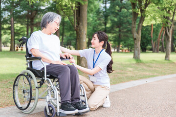 Fototapeta na wymiar 公園を散歩する車椅子の高齢者と介護士・看護師・理学療法士・運動指導員の女性 