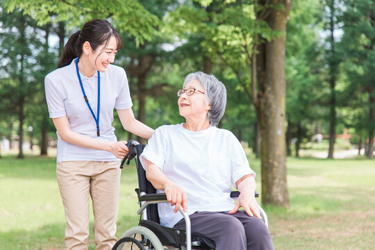 公園を散歩する車椅子の高齢者と介護士・看護師・理学療法士・運動指導員の女性
