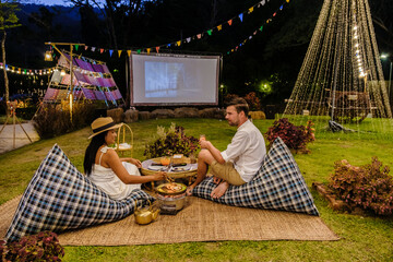 Couple men and women watching a movie in the garden of an outdoor cinema film in a tropical garden...