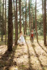 young couple bride in a white short dress and groom in a gray suit in a pine forest