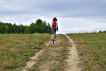 A young tourist is walking along a path in the middle of the forest with her dog