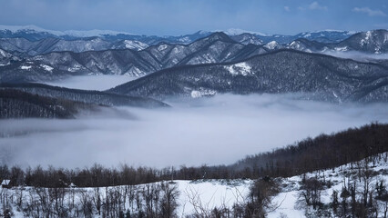 Fog in the valley, between the snow mountains in winter.