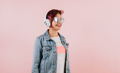 young hispanic woman girl listening music with headphones and holding mobile phone on coral pink background with copy space studio portrait in Mexico Latin America	