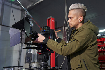 caucasian cameraman with hair adjusts focus on professional movie camera on set