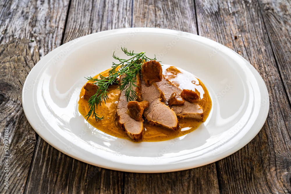 Poster fried veal loin in chanterelle mushrooms sauce on wooden table