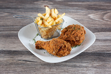 A view of a plate of fried chicken drumsticks and french fries.