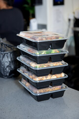 A view of a stack of food orders packed inside plastic to-go containers on the counter.