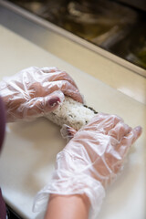 A view of hands preparing a sushi roll at an ingredient station.