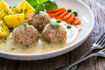 Boiled meatballs in dill sauce with potato puree, carrots and peas on wooden table

