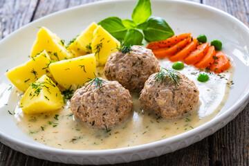 Boiled meatballs in dill sauce with potato puree, carrots and peas on wooden table
