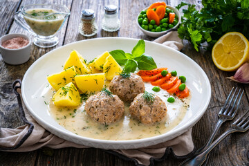 Boiled meatballs in dill sauce with potato puree, carrots and peas on wooden table
