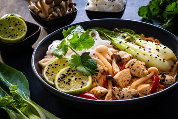 Tom Yum - Thai soup with chicken breast nuggets and noodles on wooden table

