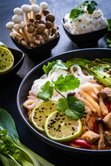 Tom Yum - Thai soup with chicken breast nuggets and noodles on wooden table
