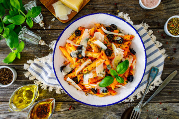 Noodles with pesto, parmesan cheese, basil and black olives served on wooden table