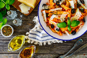 Noodles with pesto, parmesan cheese, basil and black olives served on wooden table