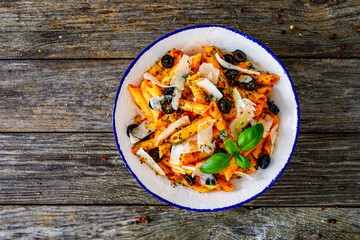 Noodles with pesto, parmesan cheese, basil and black olives served on wooden table