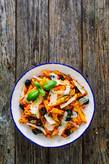 Noodles with pesto, parmesan cheese, basil and black olives served on wooden table