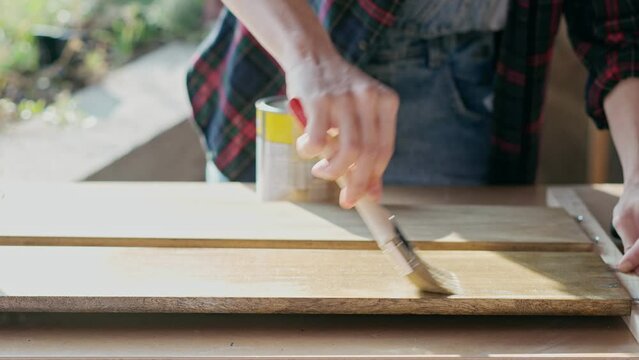 Close-up slow motion footage of a person using a brush to varnish a wooden board.