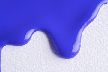 Blue liquid drops of paint color flow down on white canvas. Abstract art. Blue paint dripping on the white wall with copy space.