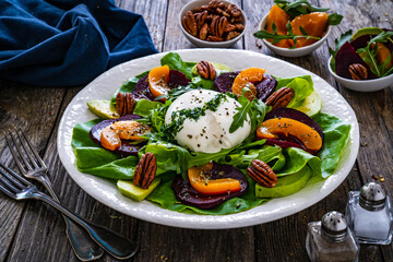 Burrata cheese with roasted beets, greens, peaches and pecan nuts on wooden table
