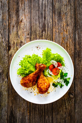 Barbecue chicken drumsticks with lettuce and tomatoes on wooden table
