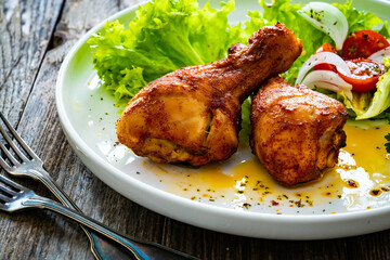 Barbecue chicken drumsticks with lettuce and tomatoes on wooden table
