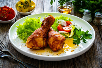 Barbecue chicken drumsticks with lettuce and tomatoes on wooden table
