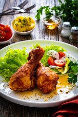Barbecue chicken drumsticks with lettuce and tomatoes on wooden table
