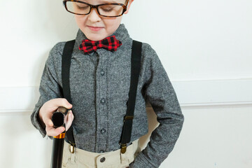 Boy dressed up as elderly man looks down at cane while wearing glasses