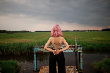 woman stands with his back near the river channel in the field