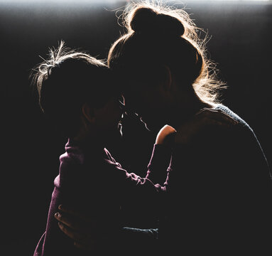 Backlit portrait of mother and son with heads together smiling.